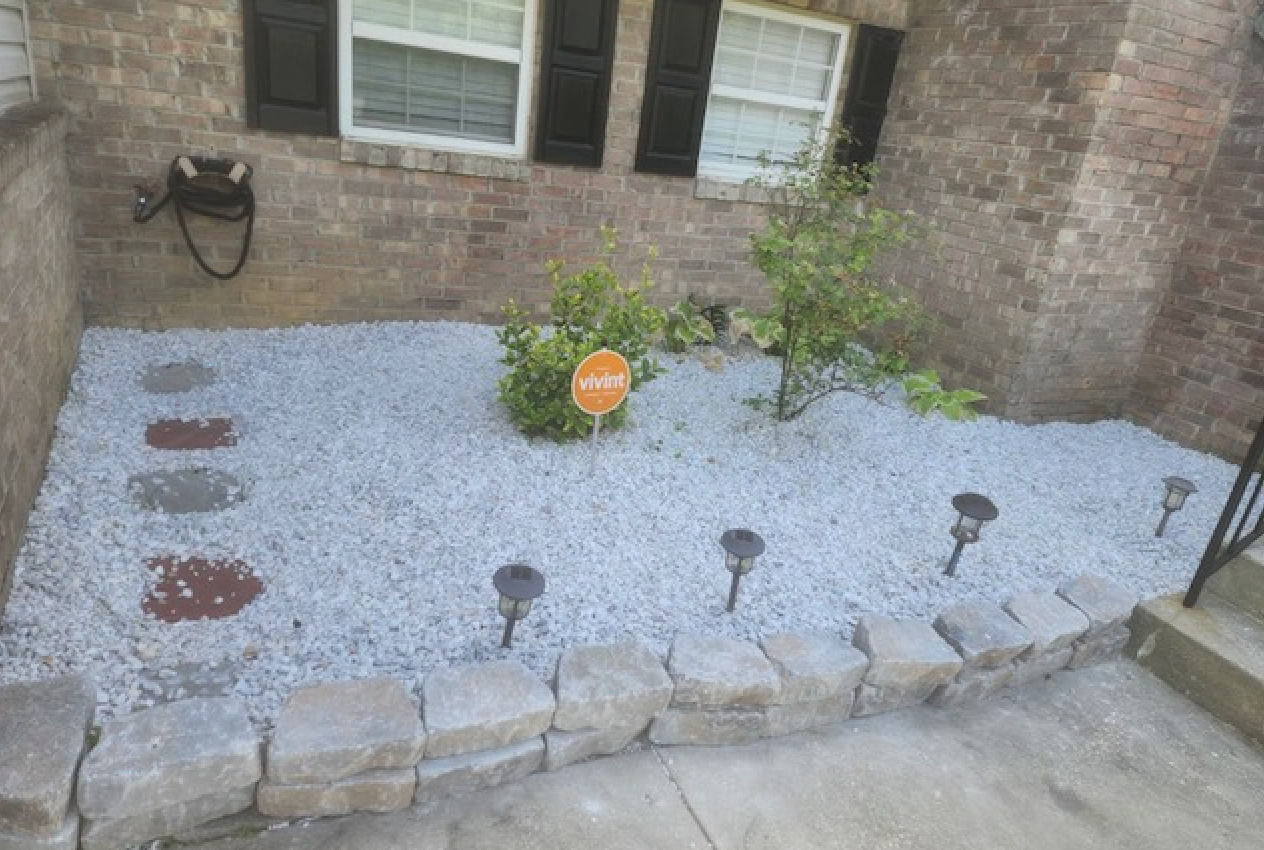 A garden with gravel and solar lights in front of a brick house.