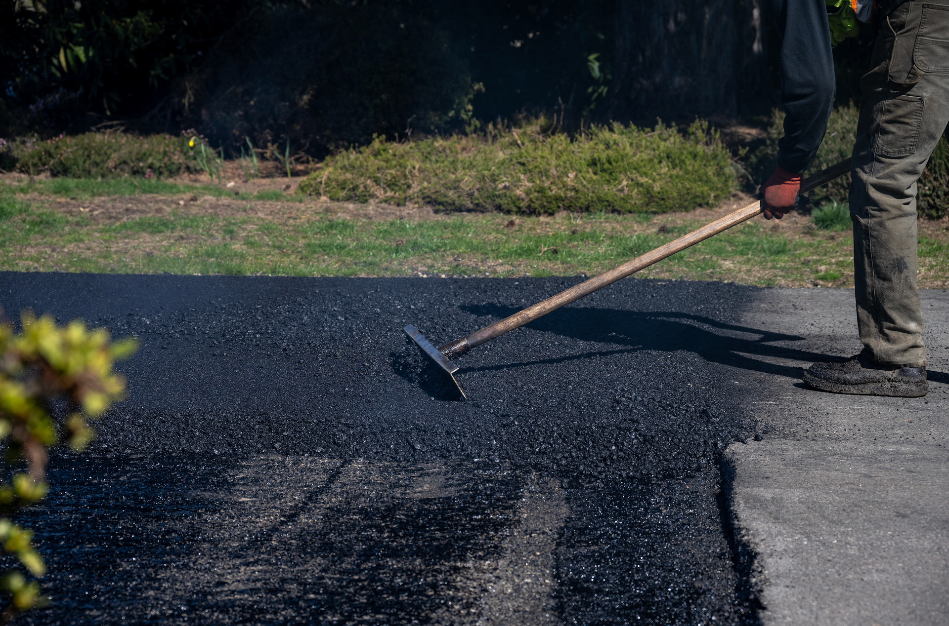 A man is spreading asphalt on a driveway with a rake.