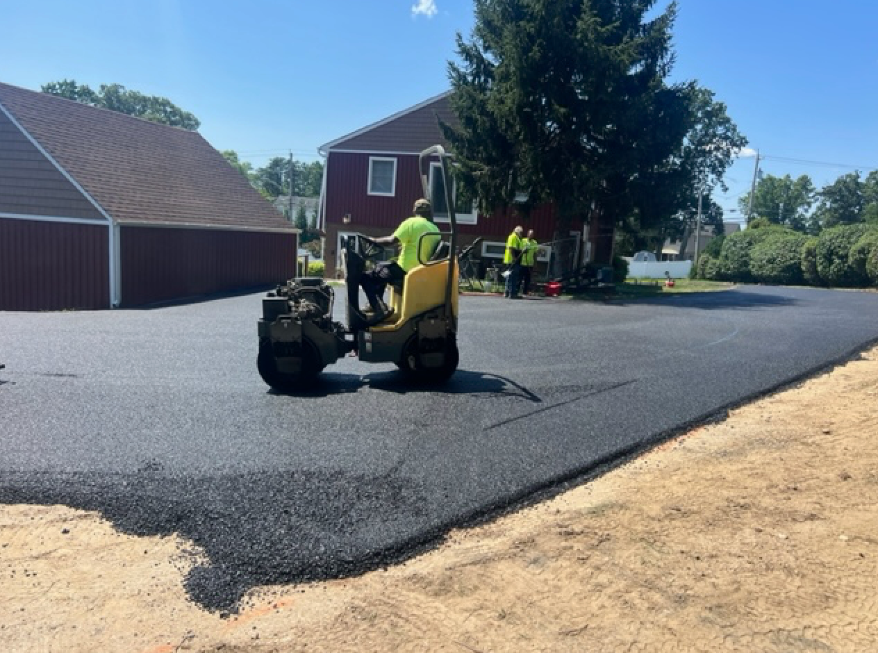 A man is driving a yellow roller on a driveway