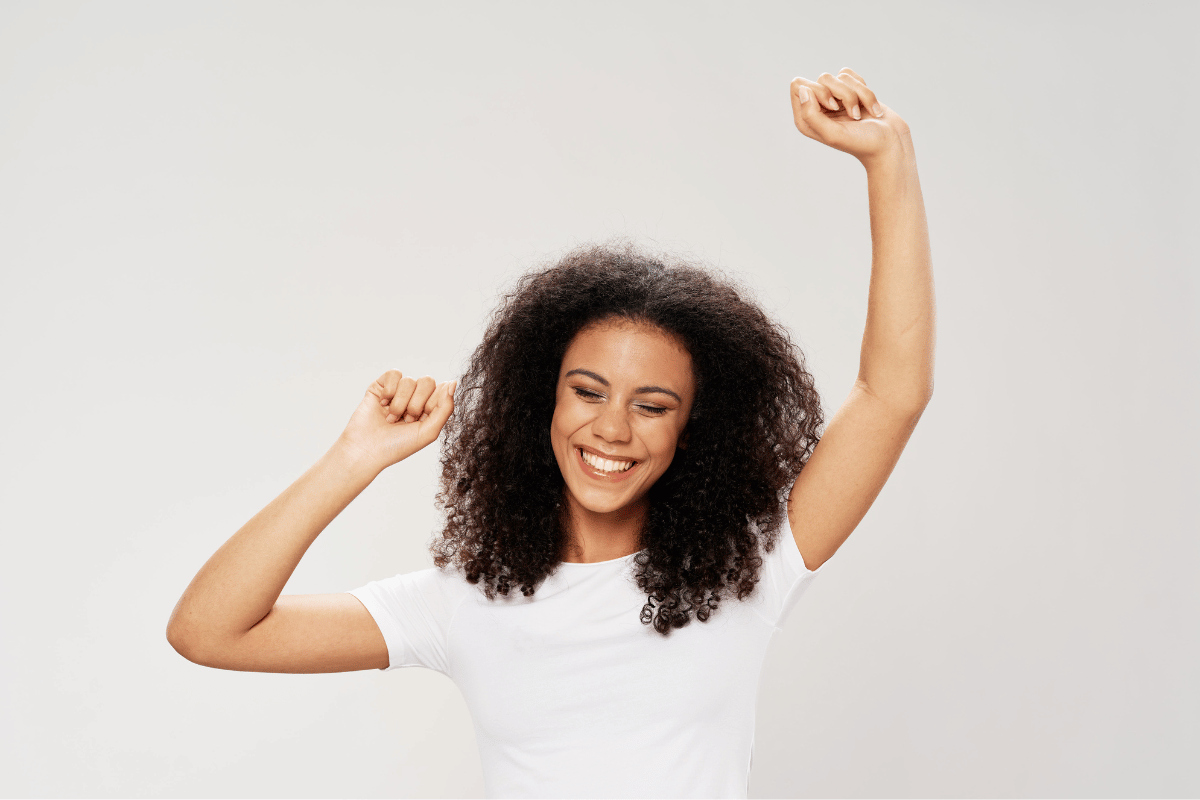 Woman with curly hair smiling, arms raised in celebration.