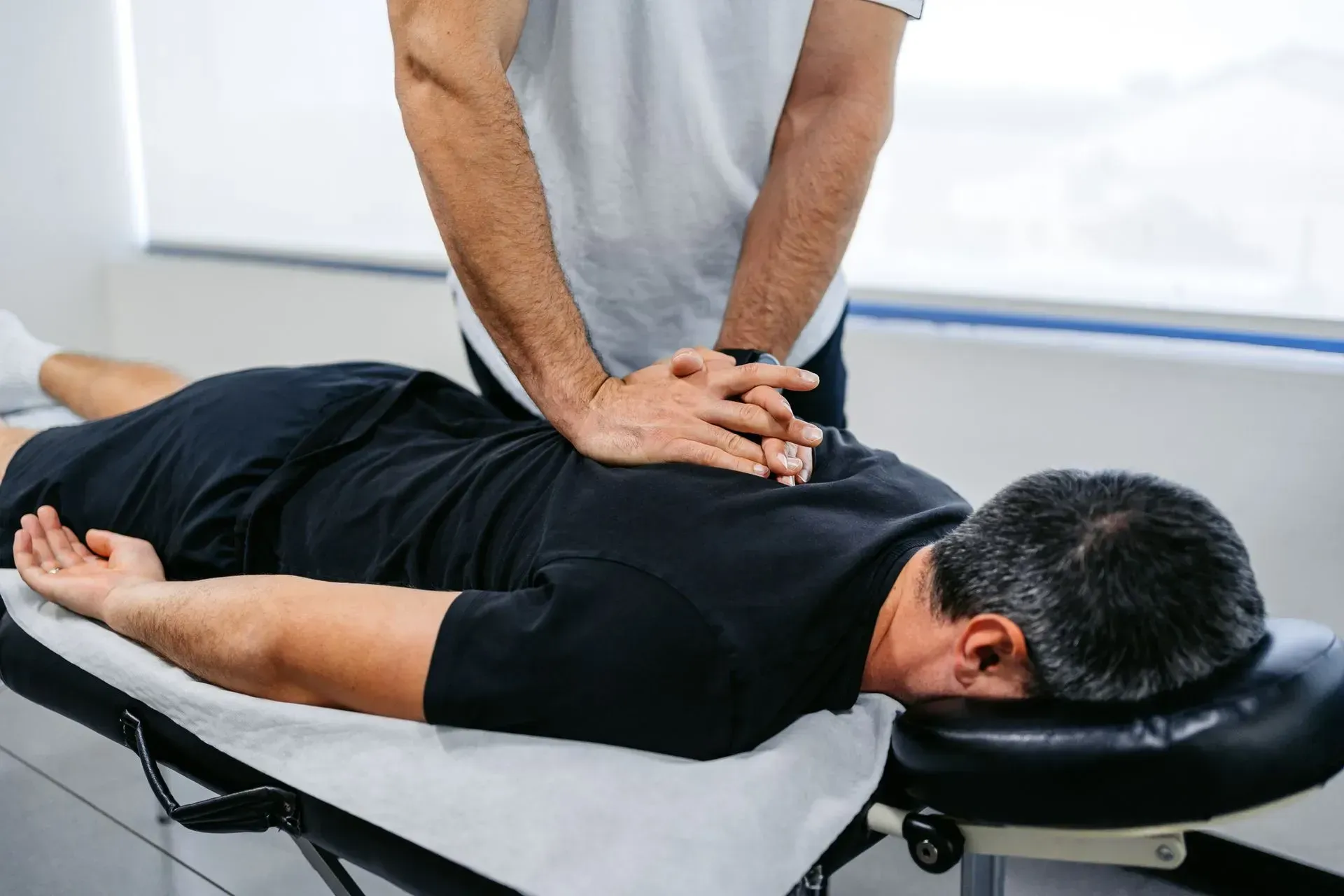 Chiropractor adjusting a patient's back, hands on the patient's spine. In a clinic setting, patient is lying on a table.