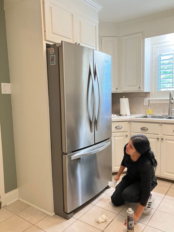 A woman is kneeling in front of a refrigerator in a kitchen.