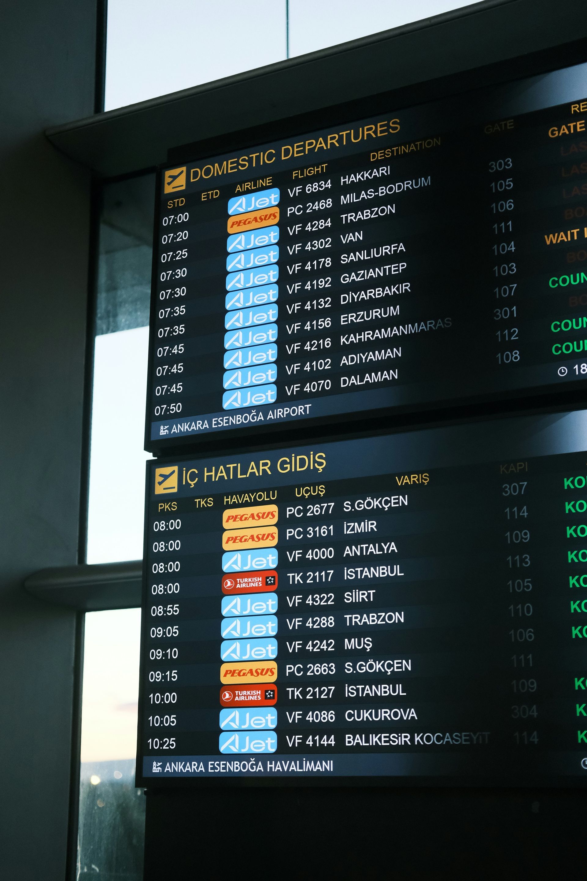 Airport departure boards with flight information; dark background, illuminated text, blue and orange highlighted rows.
