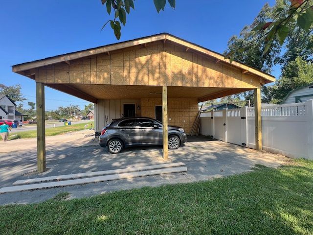 A carport with a gray car parked underneath. The structure is wood and beige.