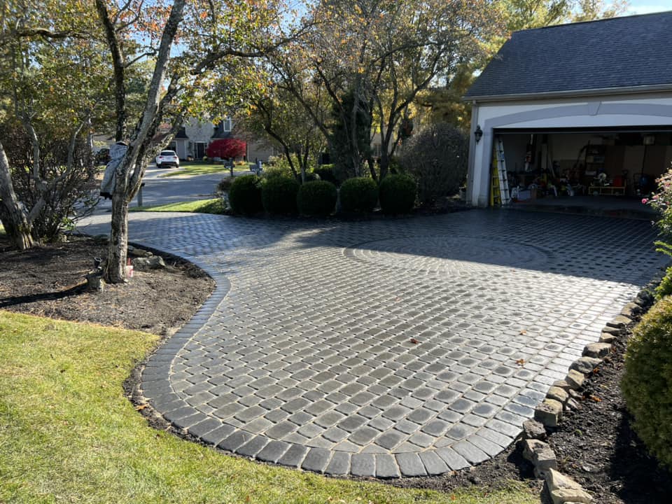 Brick driveway curves to a garage, bordered by grass and landscaping.