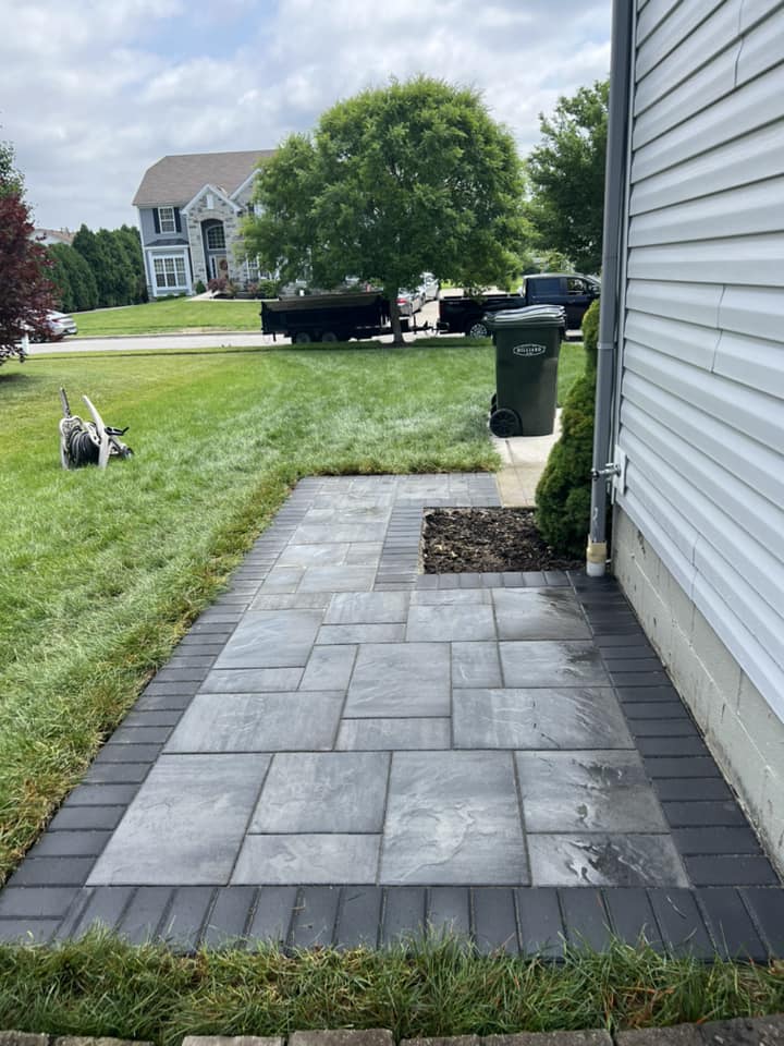 Stone patio next to a house with a dark border and adjacent grass.