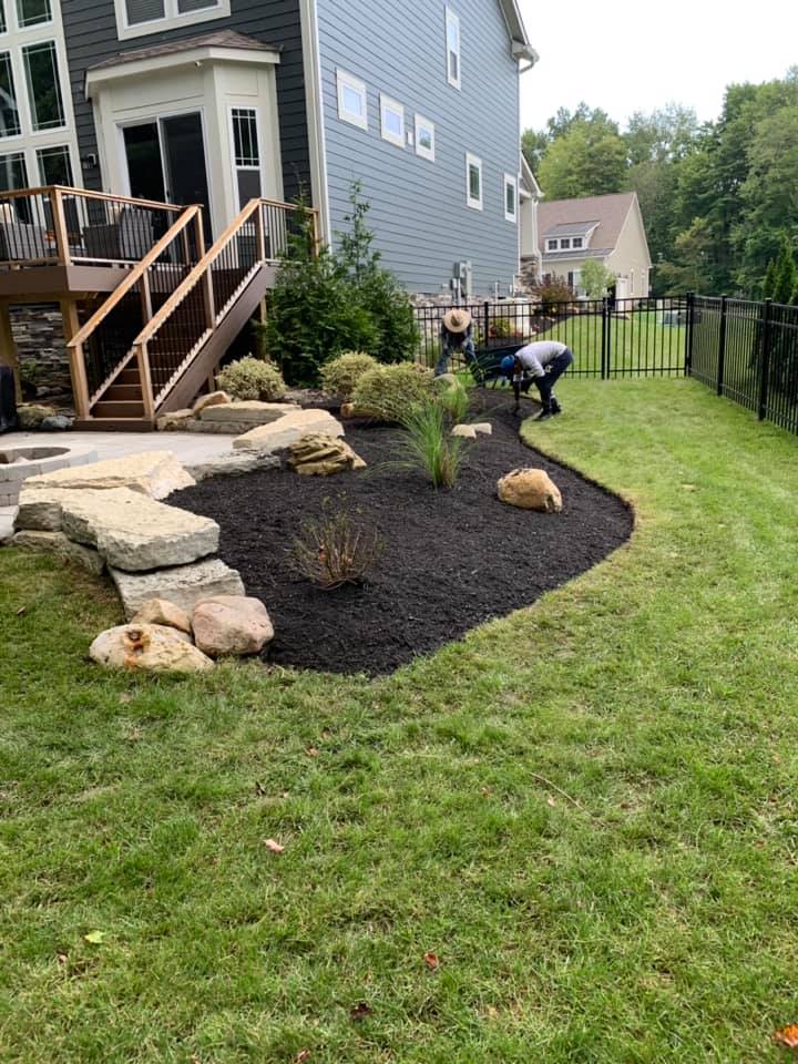 Backyard landscape with fresh black mulch, stone border, and a person working near the grass.