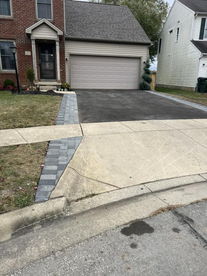 Driveway of a house with gray paved edging and a gray garage door. The driveway leads to the road.