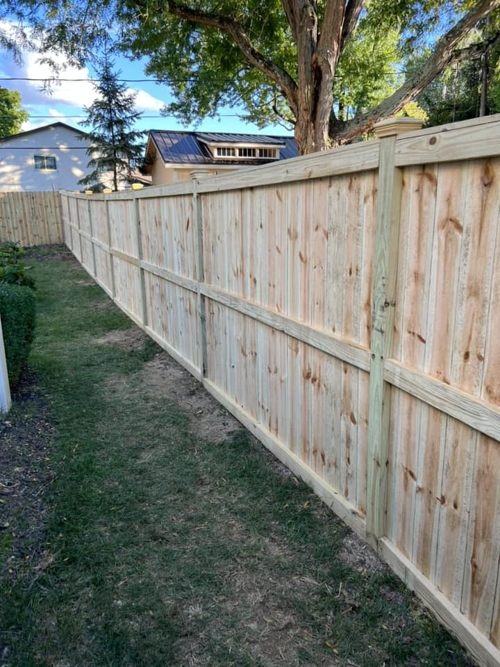 Wooden fence in backyard, on a grassy area, trees in the background.