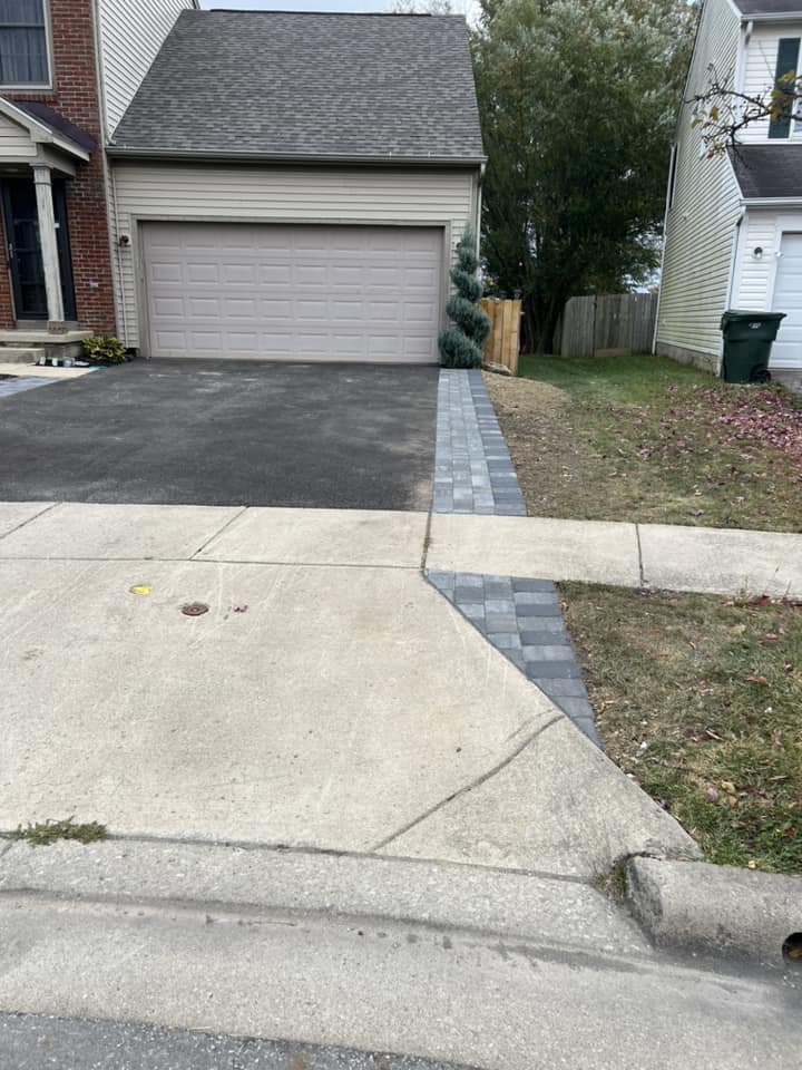 Driveway with gray garage door, patterned stone walkway, and asphalt and concrete surfaces.