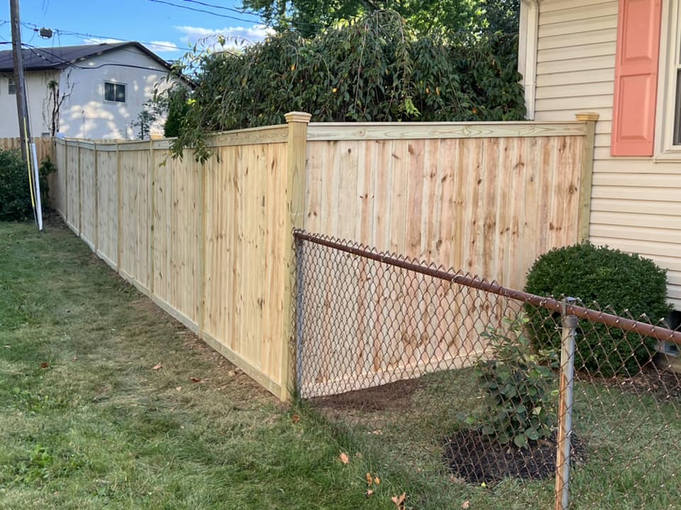 Wooden fence bordering a grassy yard, partially obscuring a house with pink shutters.