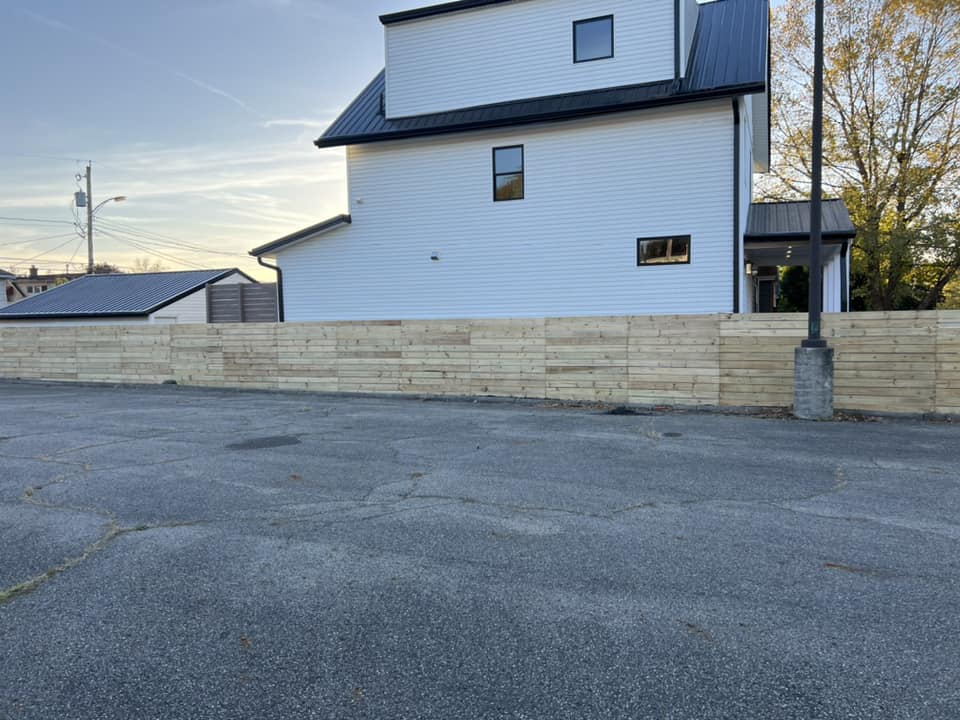 White modern house behind a long wooden fence, on a paved lot.