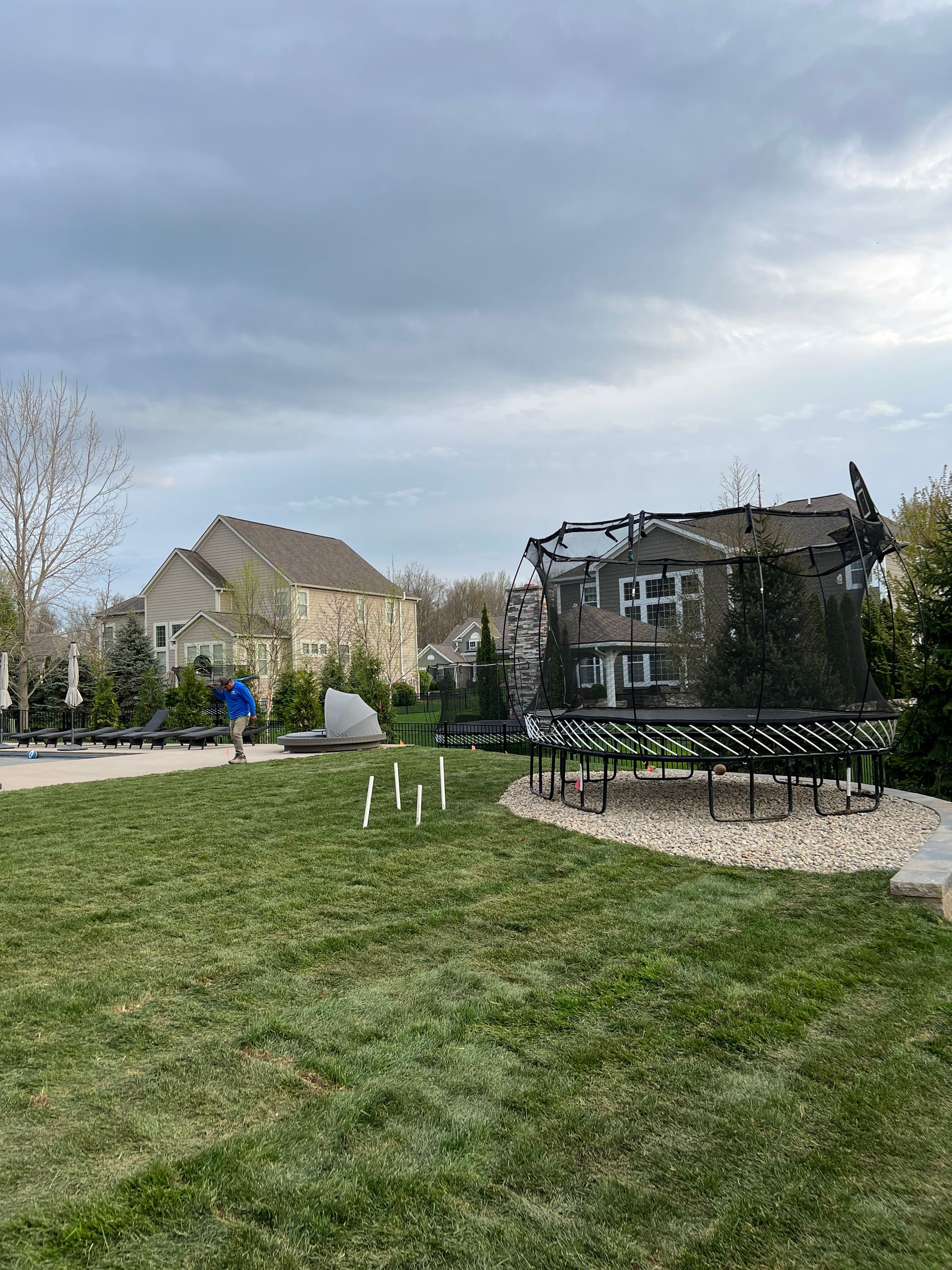 A person walks in a park with a sculpture of a partially collapsed house, cloudy sky.