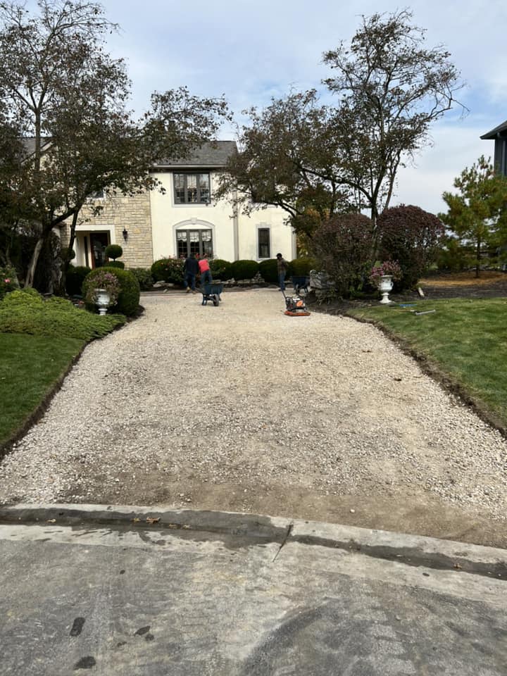 Driveway under construction in front of a house. Workers with machines flatten gravel.