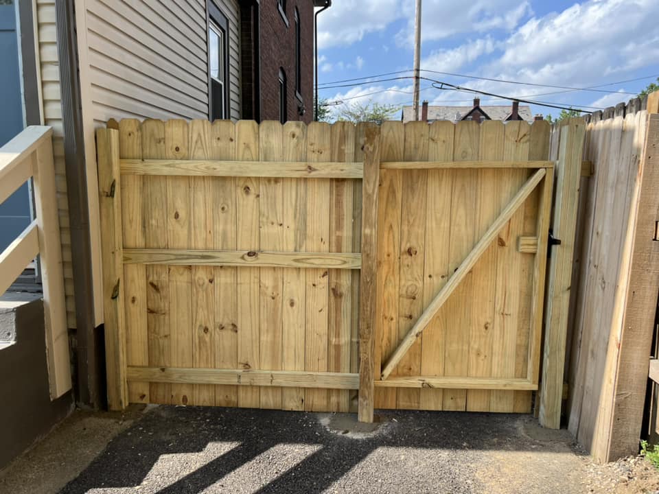 Wooden fence with gate, light brown, in front of a building. Gate has diagonal brace.