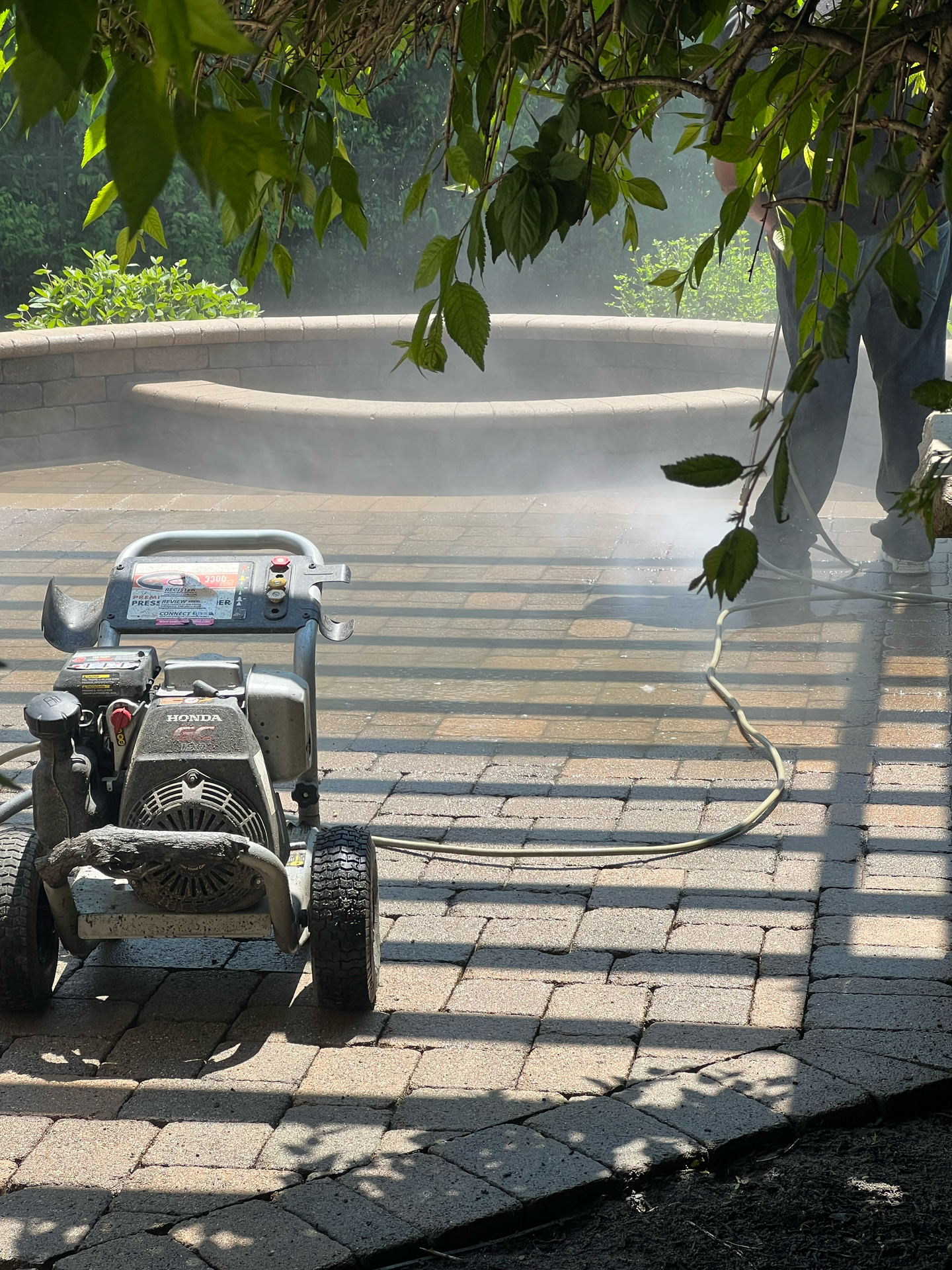 A person power washing a brick patio with a gas-powered pressure washer.