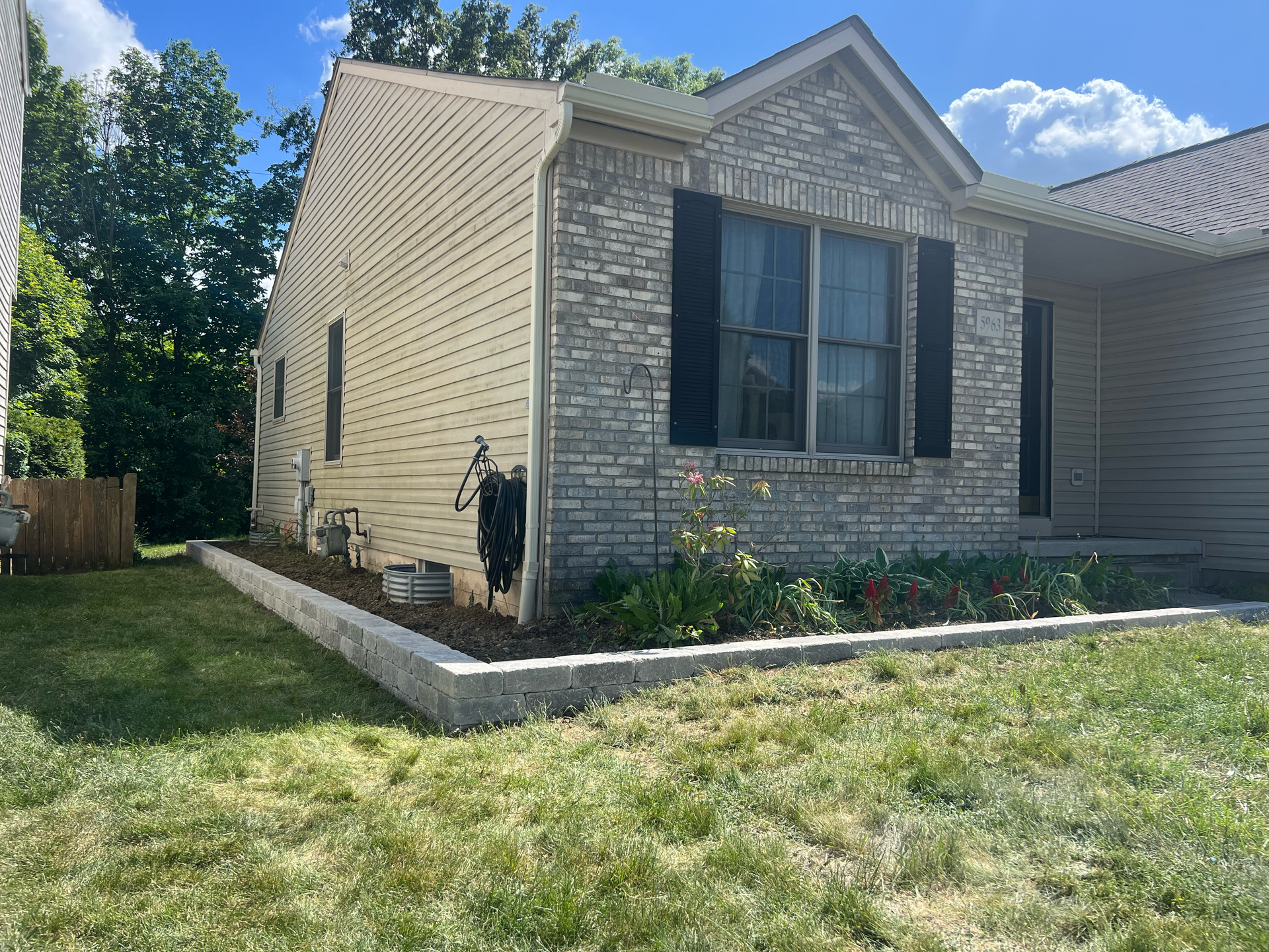 A brick and siding house with a flower bed and green grass in front.