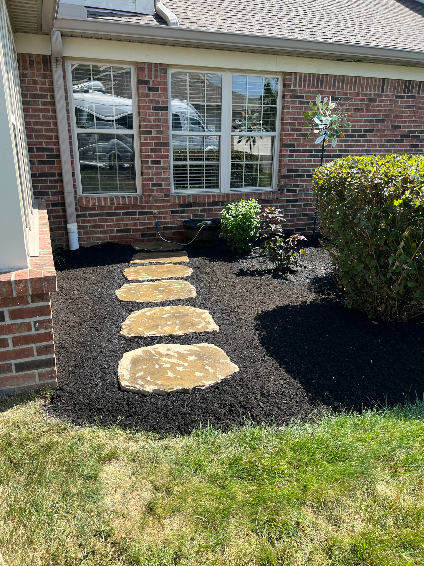 Path of stone slabs through mulched garden bed, leading to a house.