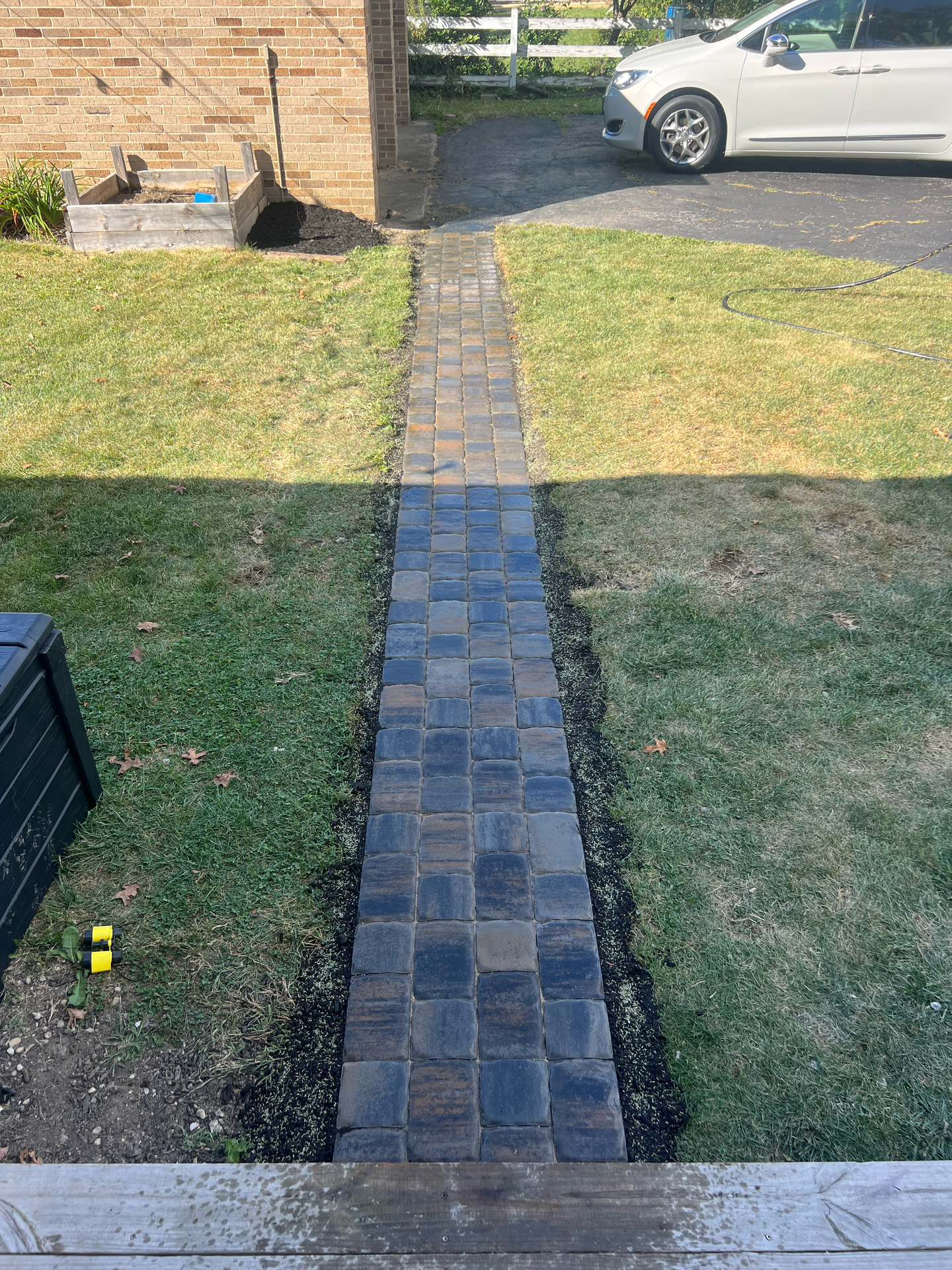 Brick walkway through grass, leading to a building. A car is parked nearby.
