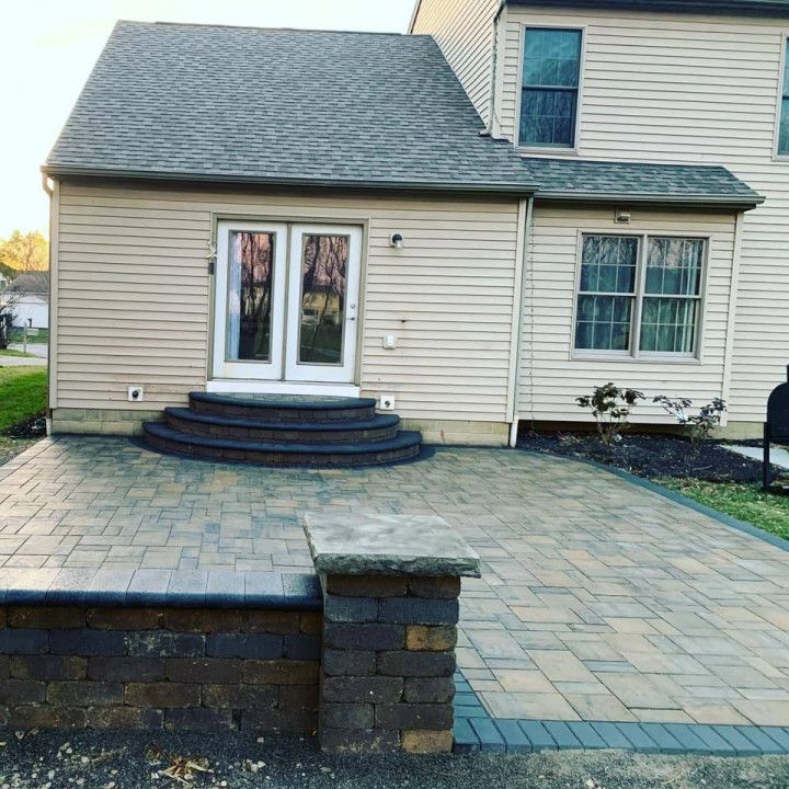 Backyard patio with pavers, low wall, steps leading to a house with French doors.
