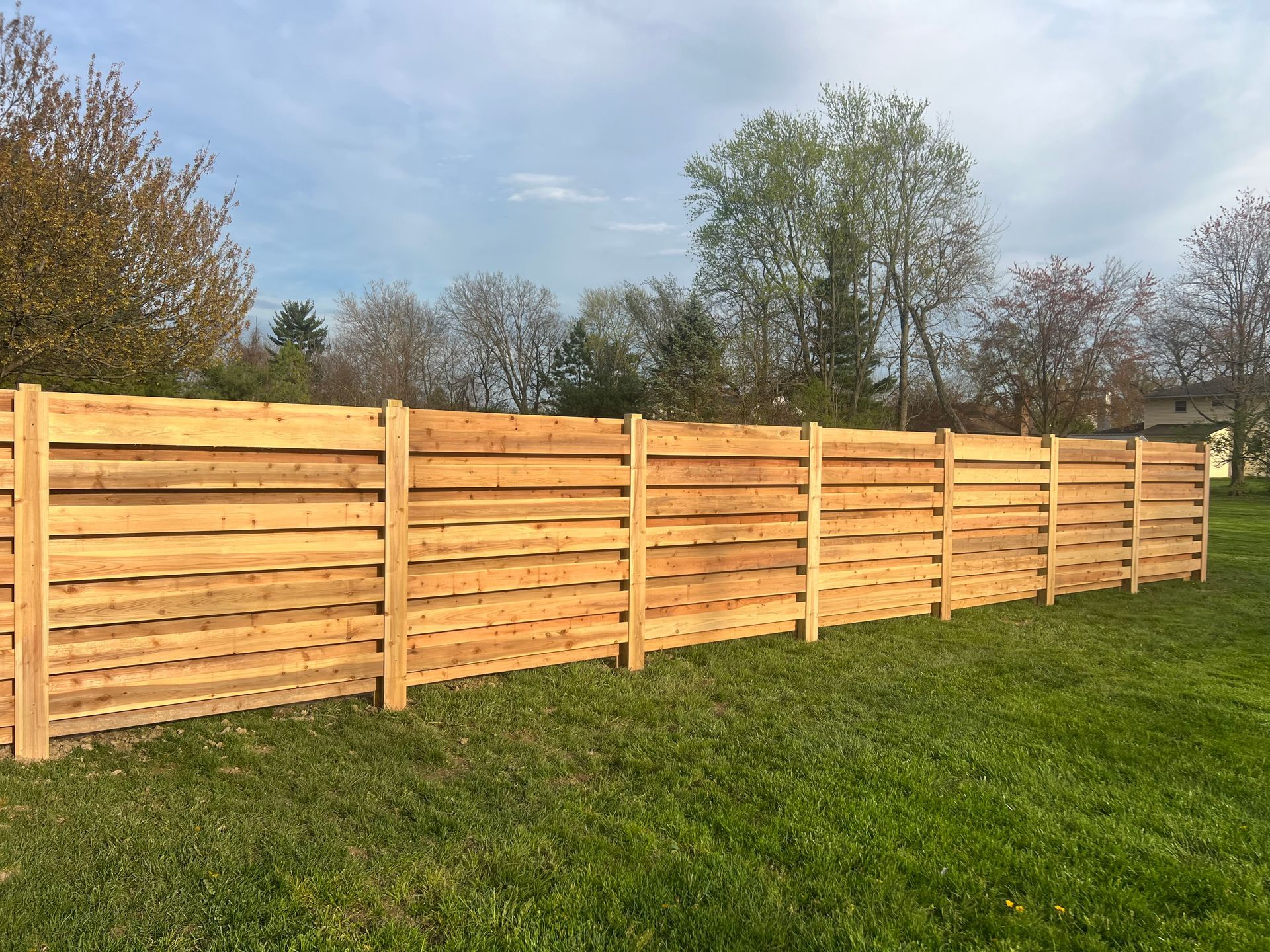 Wooden fence in a grassy yard under a partly cloudy sky.