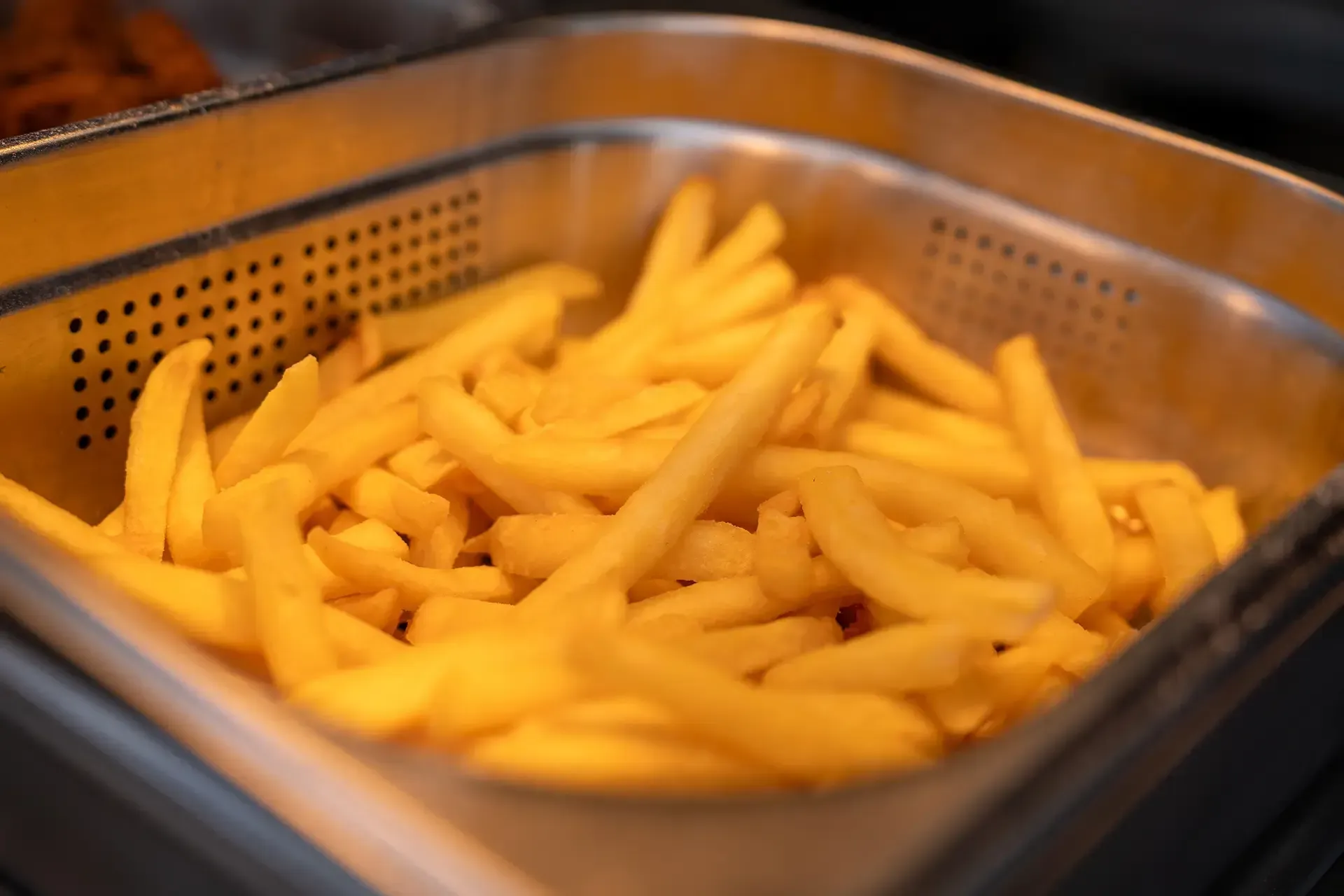A tray of french fries is being cooked in a fryer.
