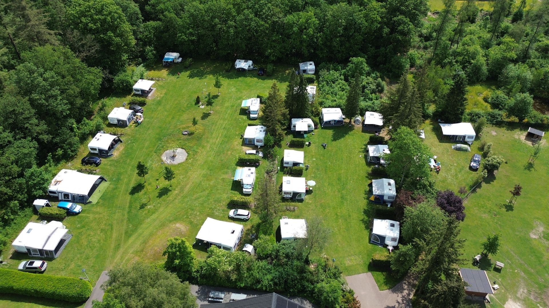 Luchtfoto van een camping met talloze campers en caravans op een groen grasveld, omgeven door bomen.