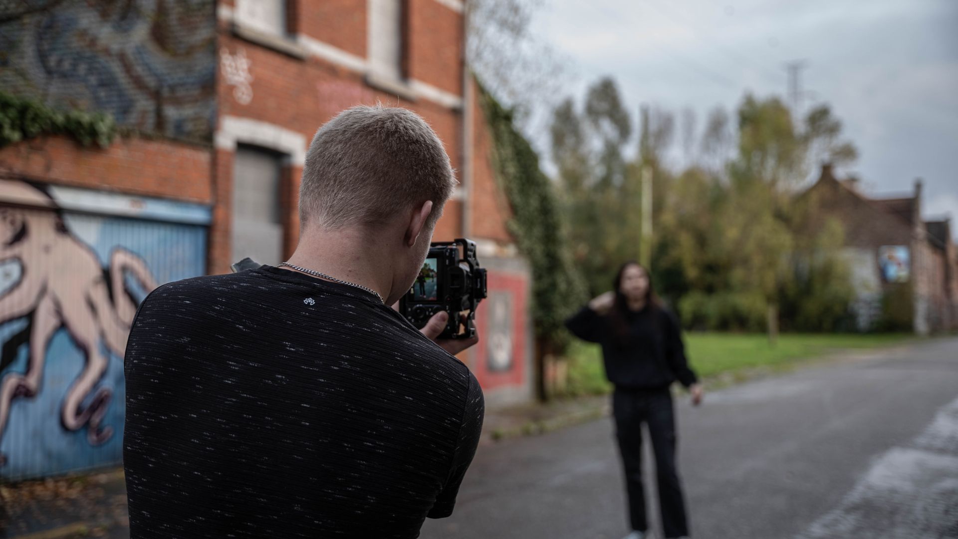 Een fotograaf filmt een persoon op straat met op de achtergrond gebouwen vol graffiti. Het is een bewolkte dag.