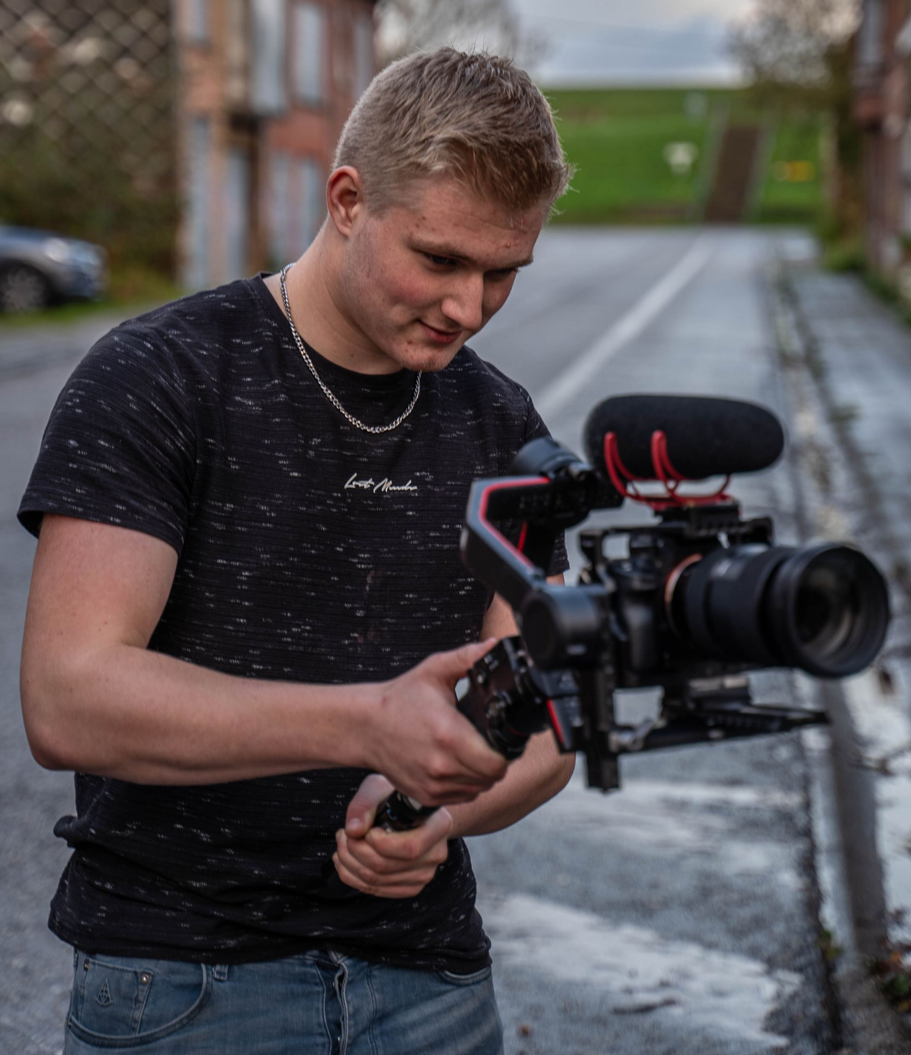 Jarno filmt met een camera op een statief in een steegje. Hij kijkt aandachtig naar beneden.