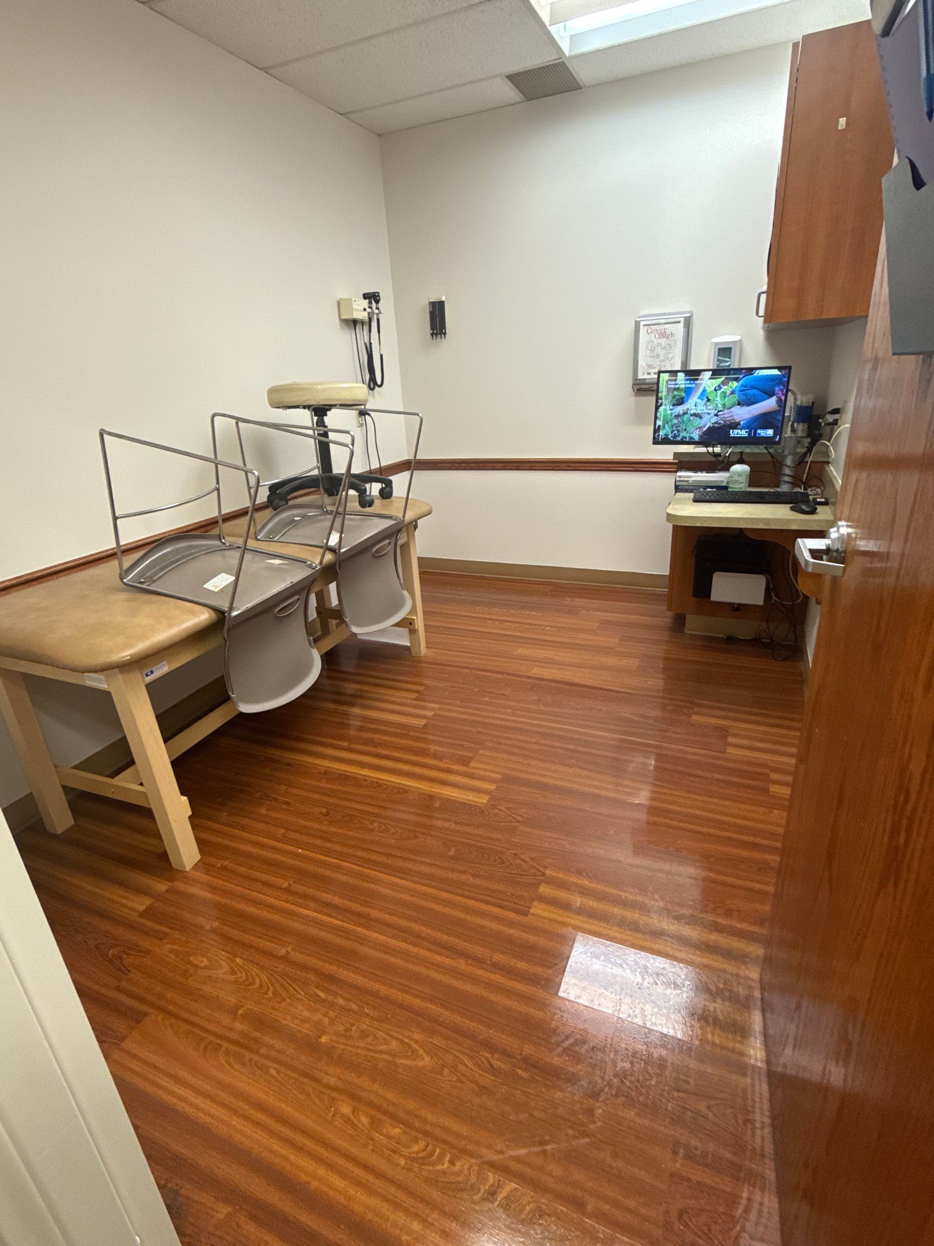 Exam room with a bed, chair, computer, and wood flooring.