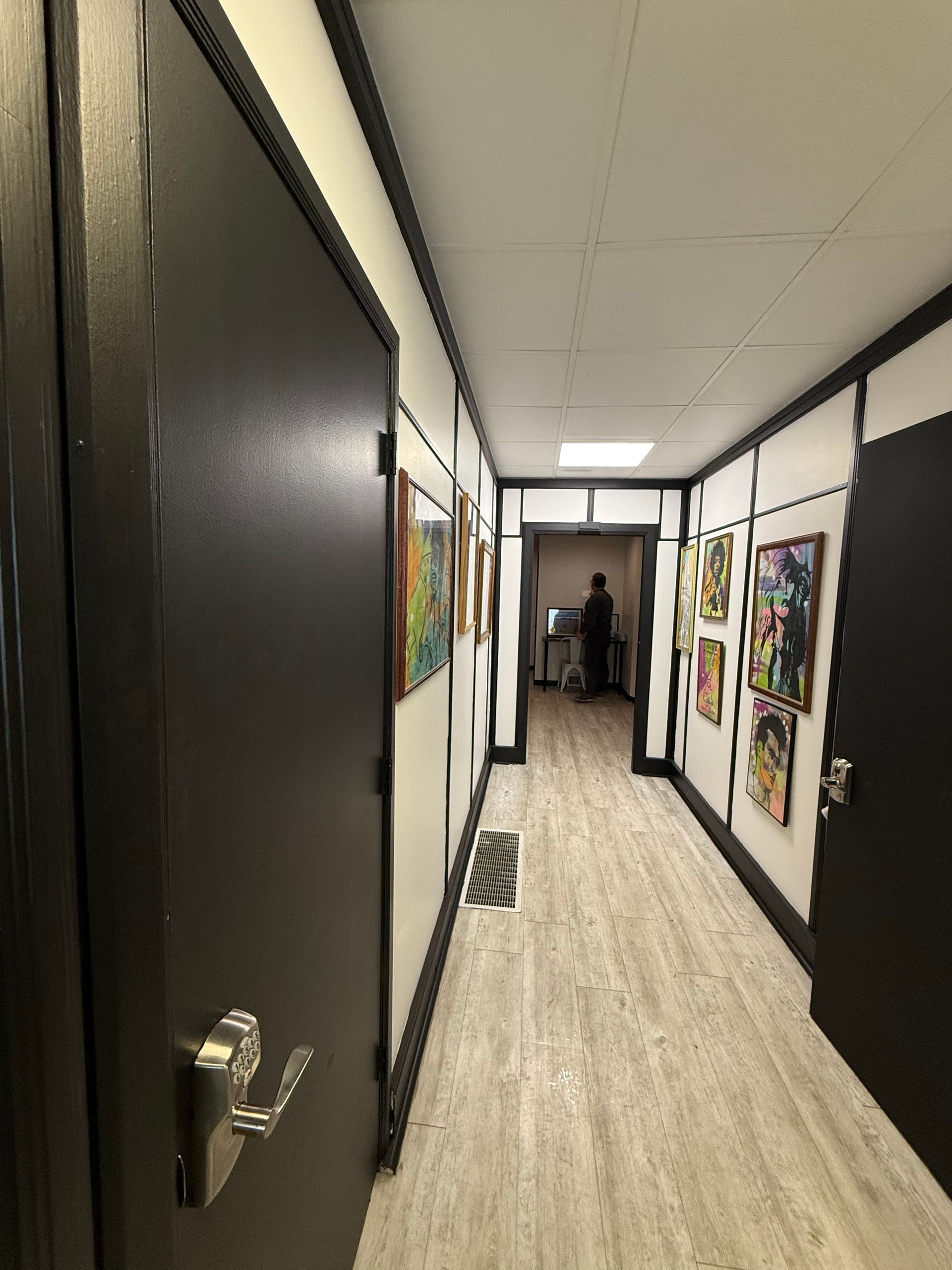 Long, narrow hallway with art, doors, and a person in the distance.