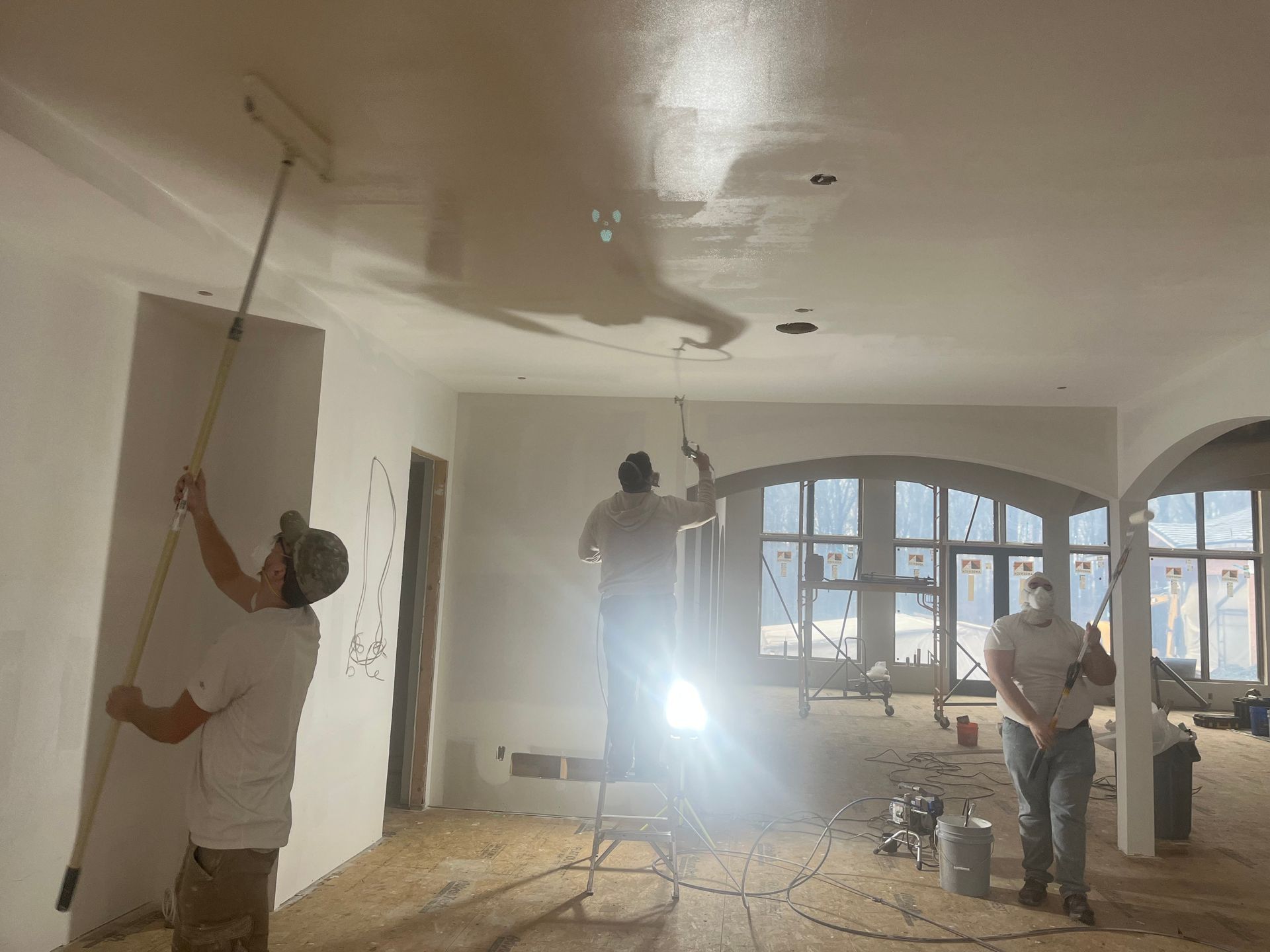Three people painting a room. One on the ceiling with a roller, two on walls. Interior construction.