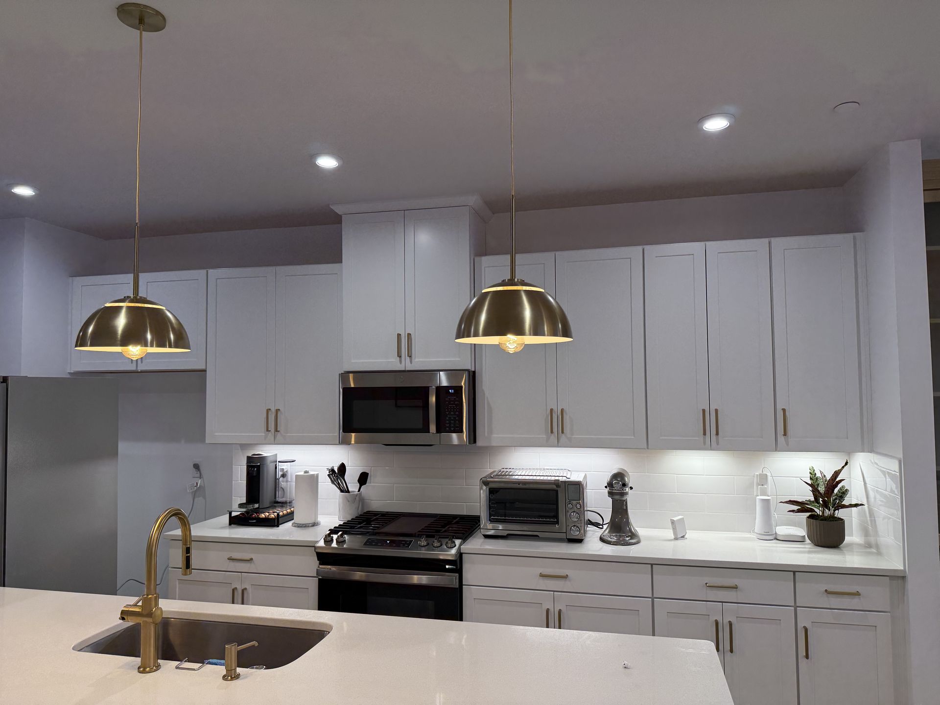 Modern kitchen with white cabinets, gold hardware and pendant lights, stainless steel appliances, and a white countertop.