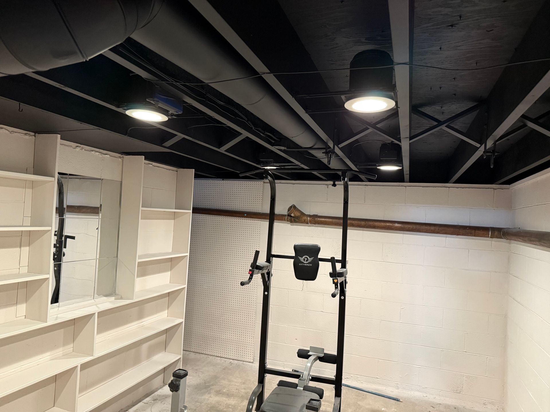 Basement with black ceiling and beams, white walls, and workout equipment.