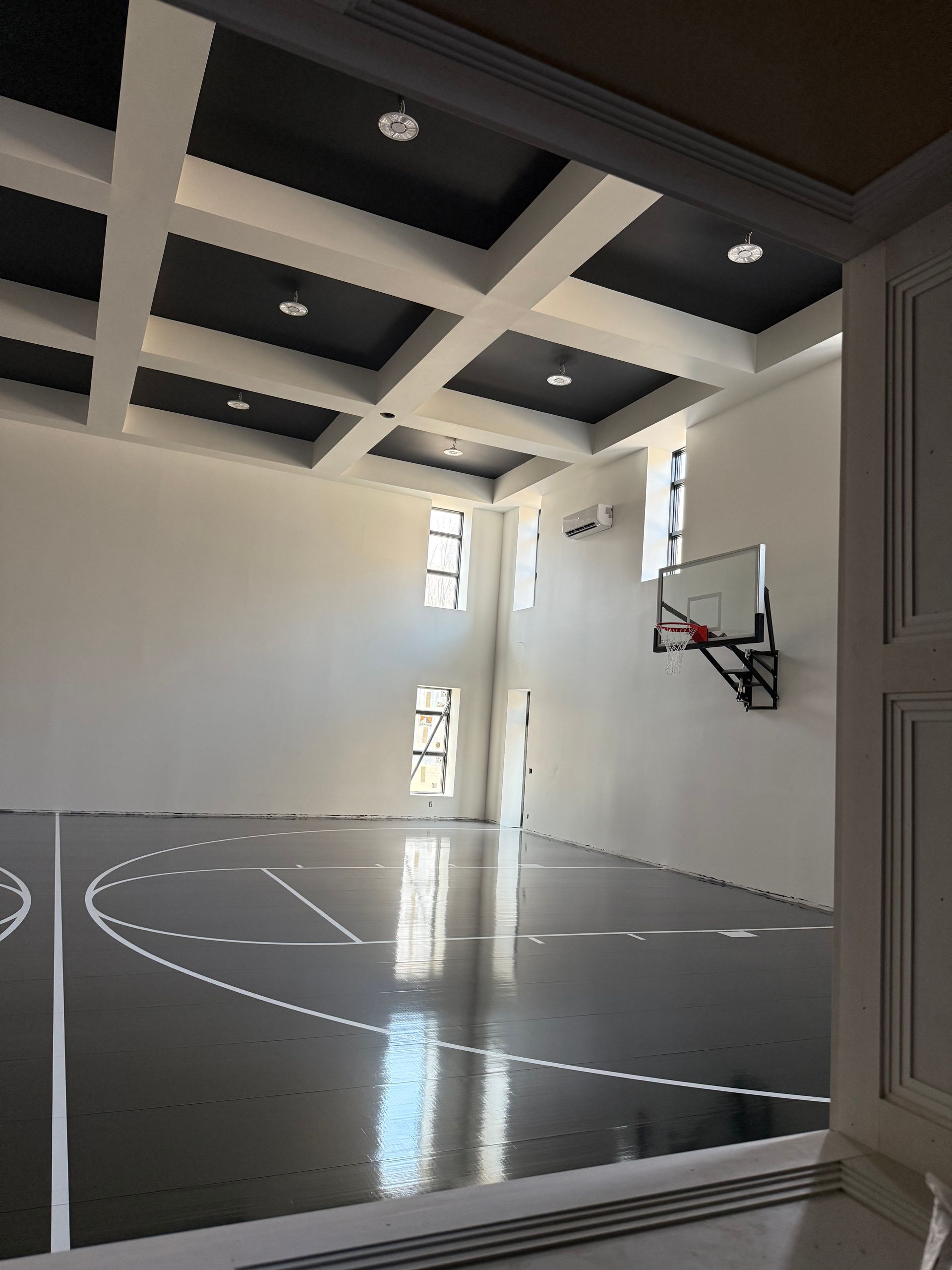 Indoor basketball court with black and white floor and ceiling design; a hoop and windows on a white wall.
