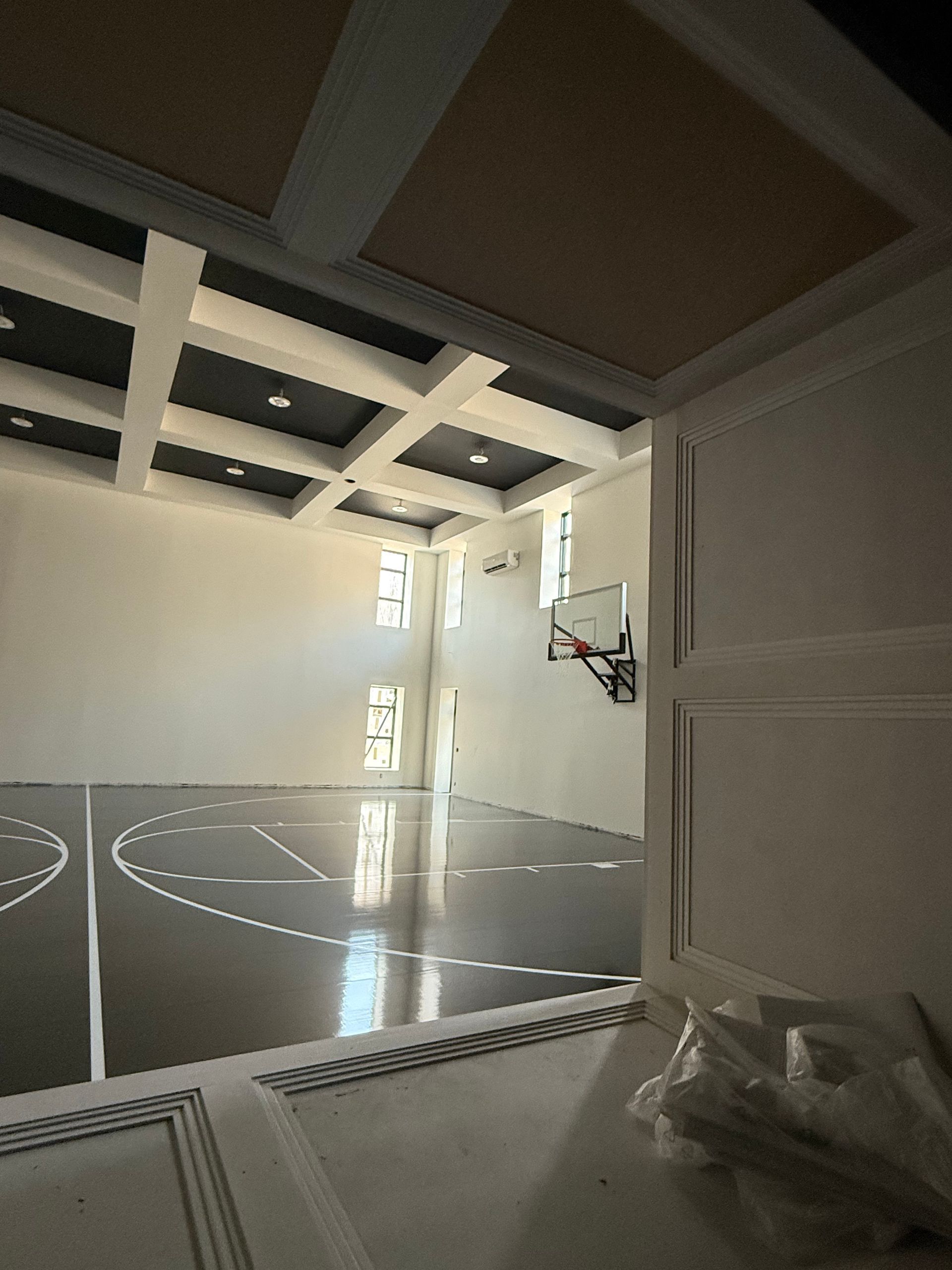 Indoor basketball court with glossy floor, ceiling grid, and hoop.