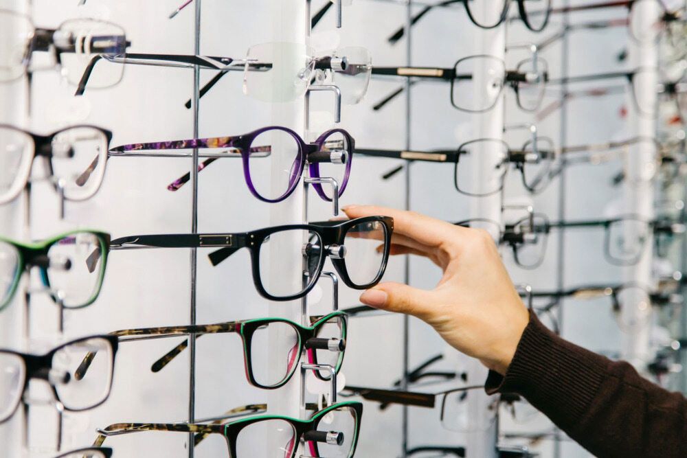 A Person Is Holding A Pair Of Glasses In Front Of A Wall Of Glasses — Eye Supply In Mareeba, QLD