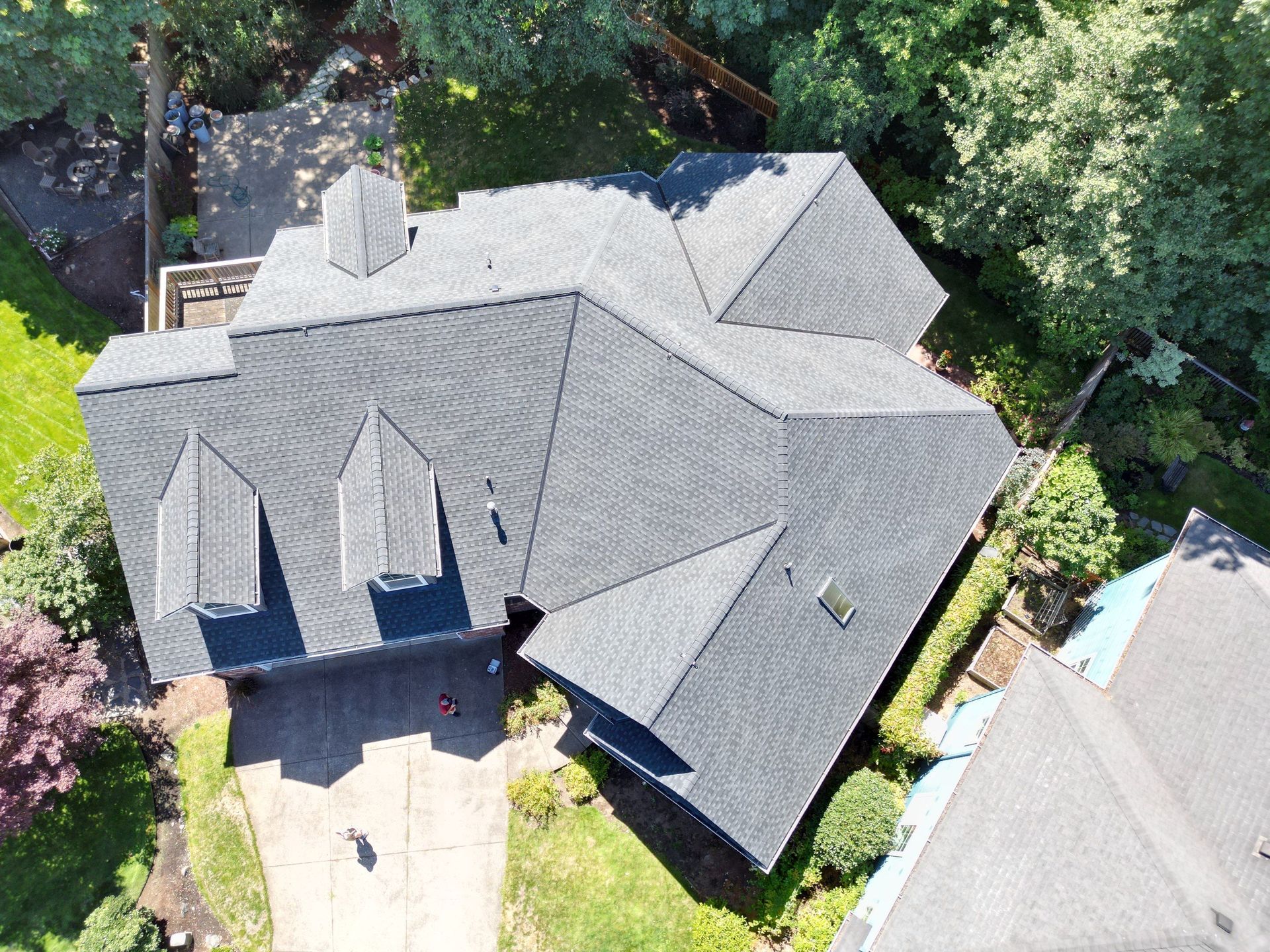 An aerial view of a house with a gray roof surrounded by trees.
