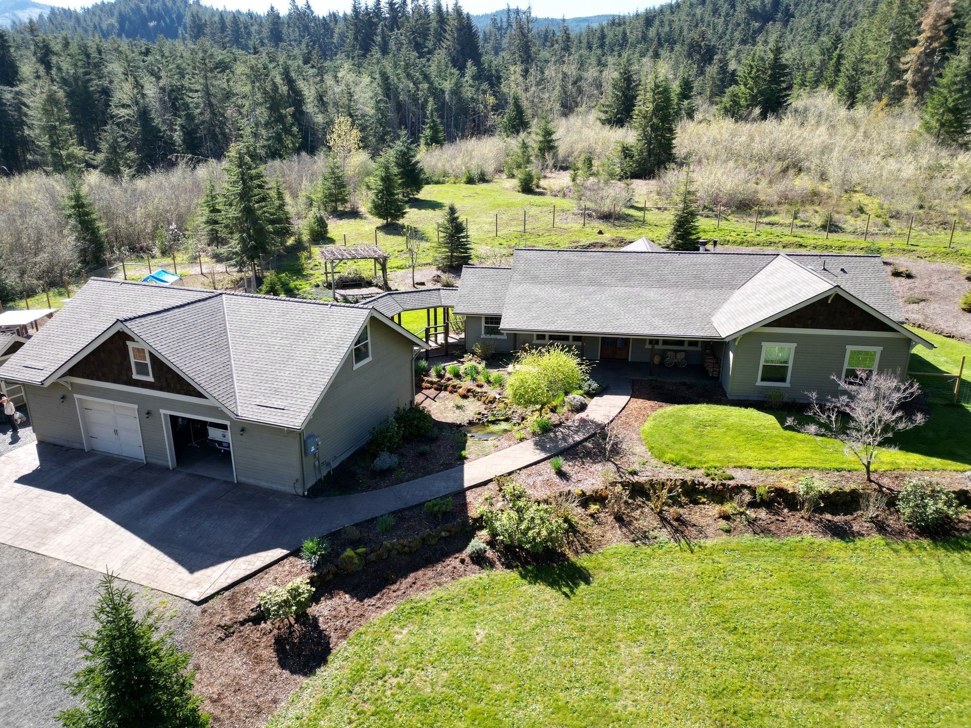 An aerial view of a house in the middle of a lush green field surrounded by trees.