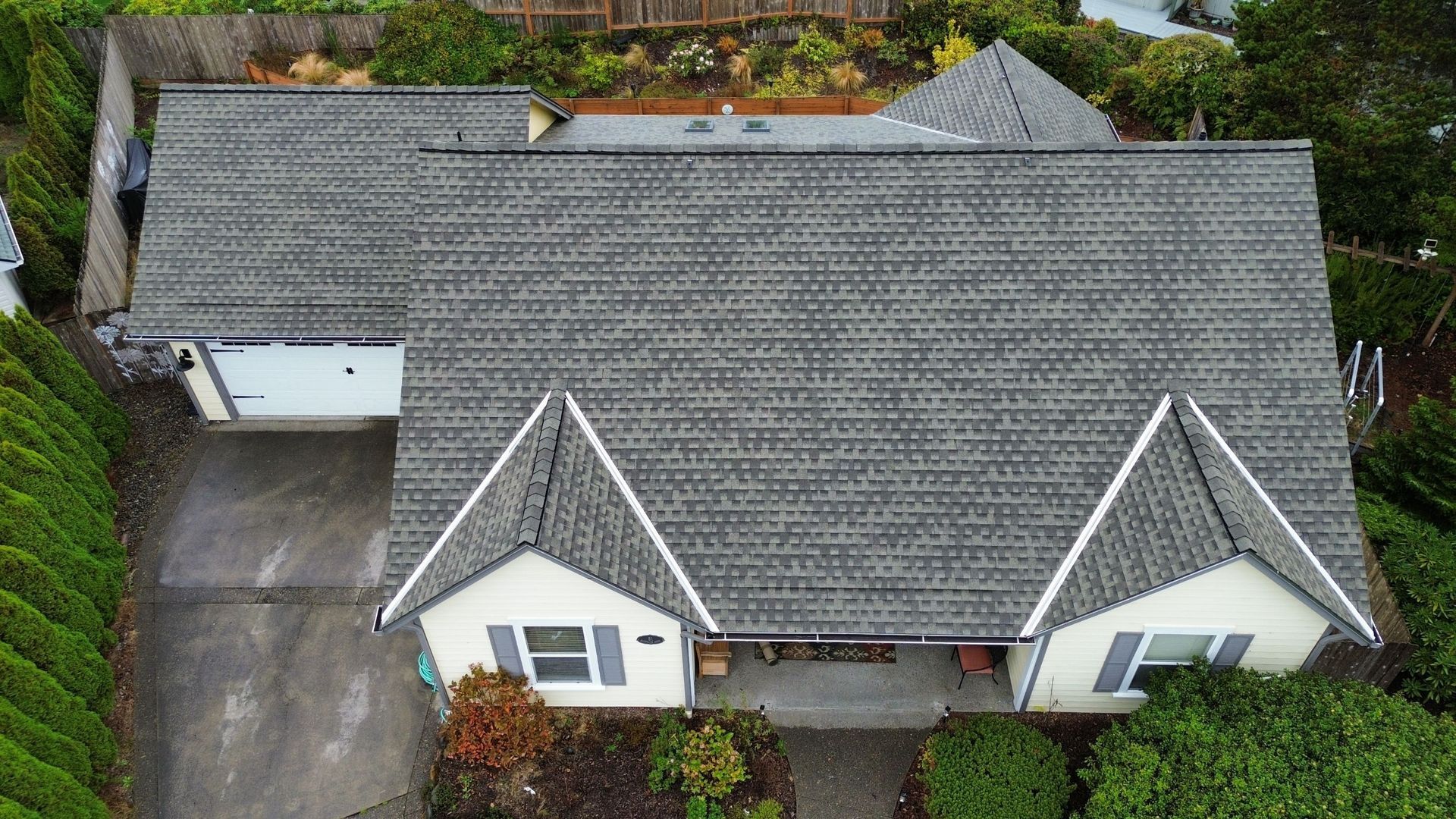 An aerial view of a white house with a gray roof surrounded by trees.