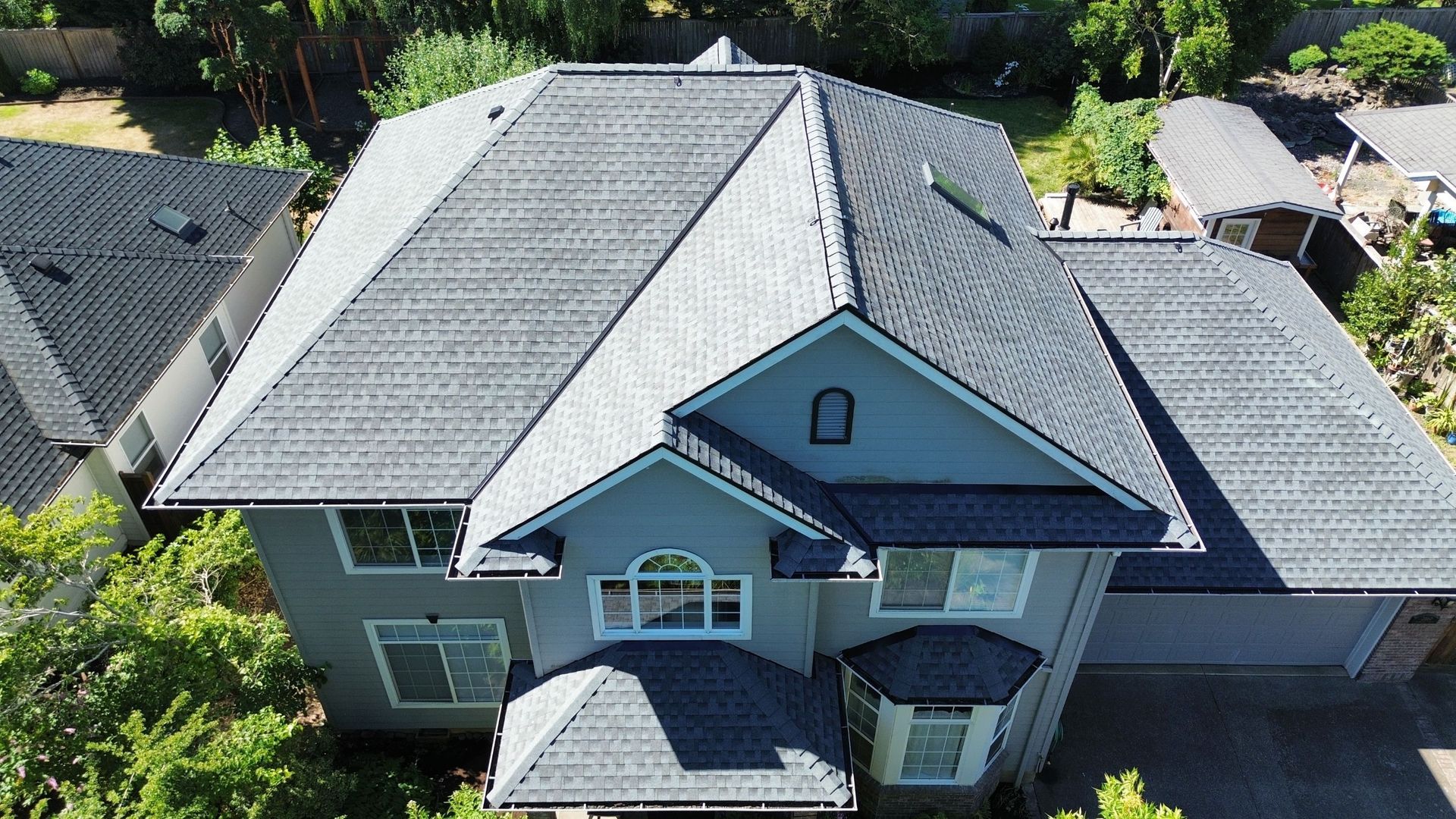 An aerial view of a large house with a gray roof surrounded by trees.