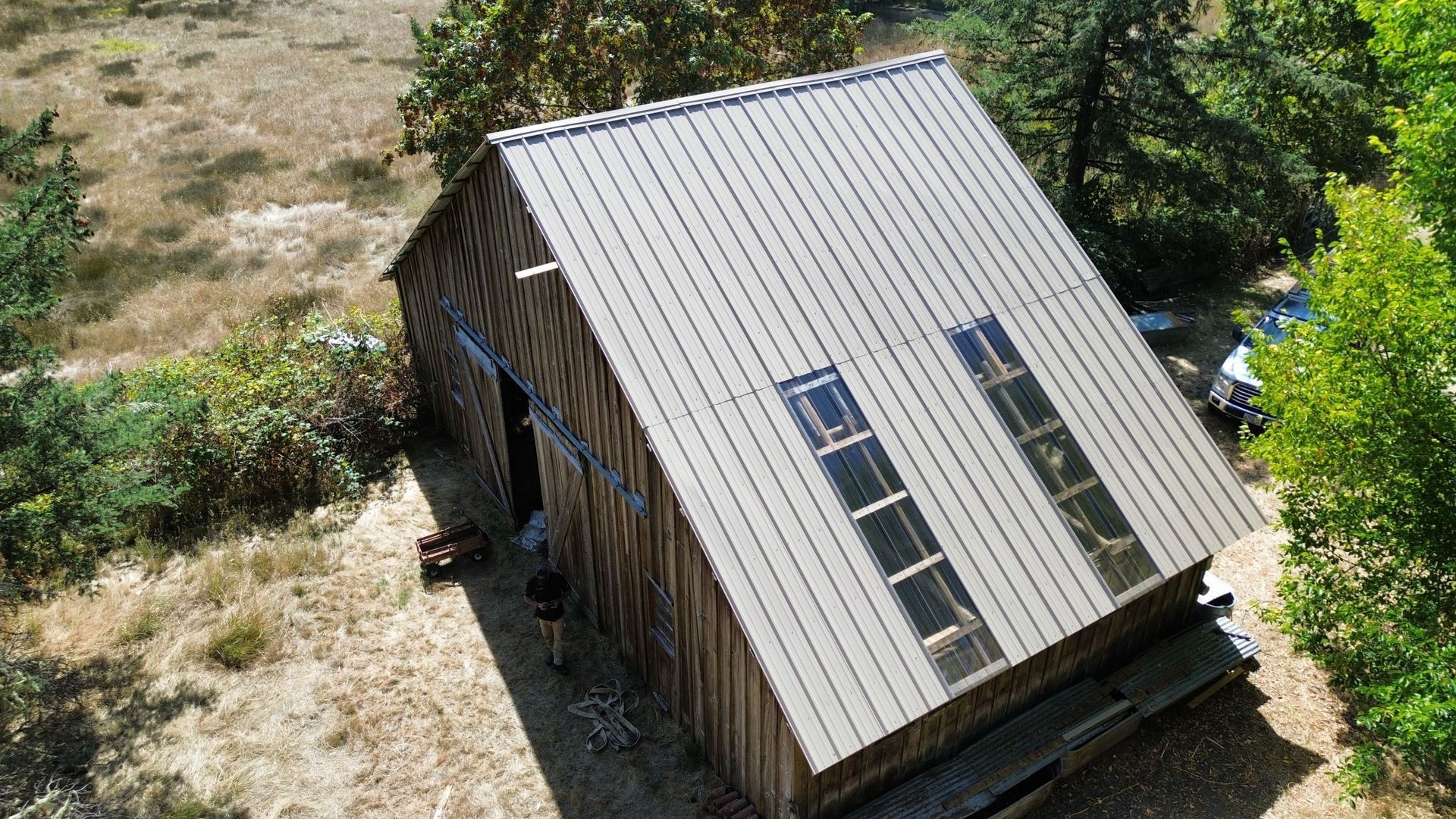 An aerial view of a small house with a metal roof surrounded by trees.