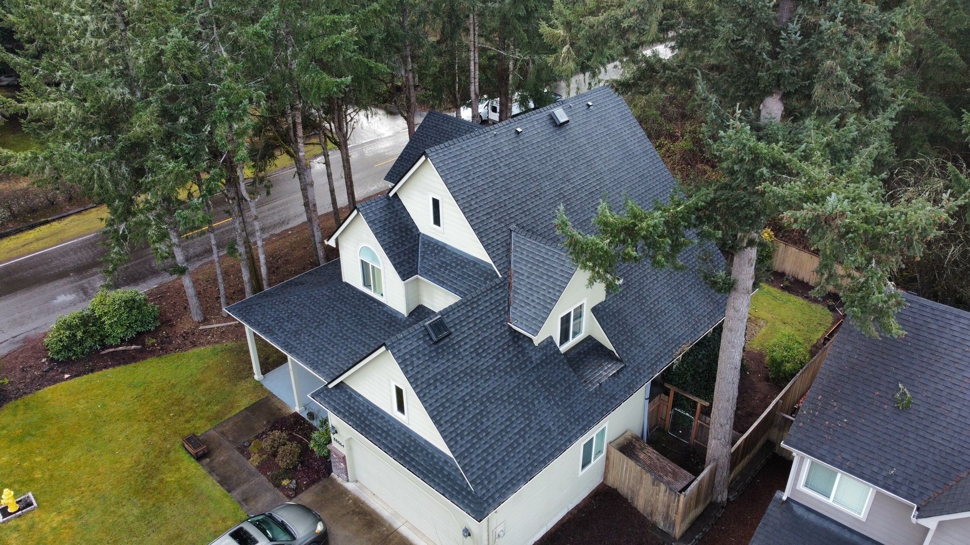 An aerial view of a house with a new roof surrounded by trees.