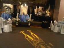 Wedding reception: tables with blue and white linens, floral arrangements, and champagne glasses projected on the floor.