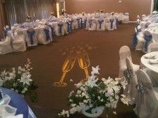 Wedding reception hall with champagne flutes projected on the floor, tables with white flowers, and blue and white decor.