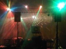 DJ setup with speakers, lights, and a disco ball, illuminated with red, green, and blue beams.