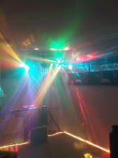 Disco lights illuminate a room, focused on a DJ setup, with colorful beams and a light-up floor border.