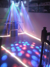 DJ setup with spotlights casting blue, green, and red beams, illuminating the floor and equipment.