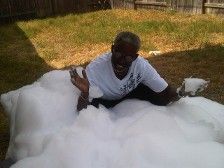 Person laughing, covered in white foam outdoors, on the grass.