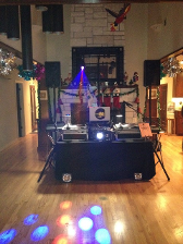 DJ setup in a home with speakers, turntables, and lights. Wooden floors, decorated fireplace, and a festive atmosphere.